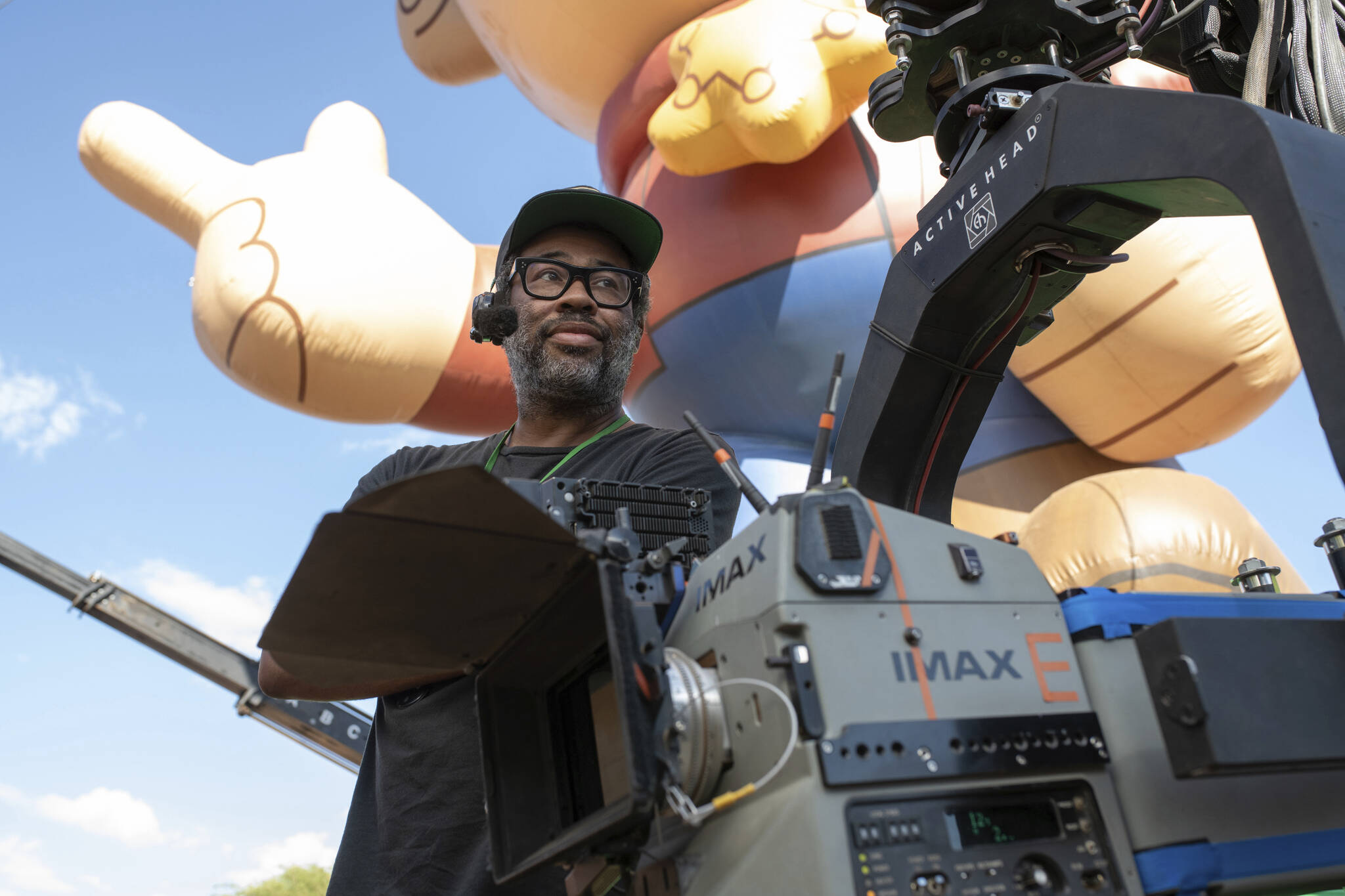 Jordan Peele stands behind an IMAX rig and a large inflatable child on the set of NOPE.