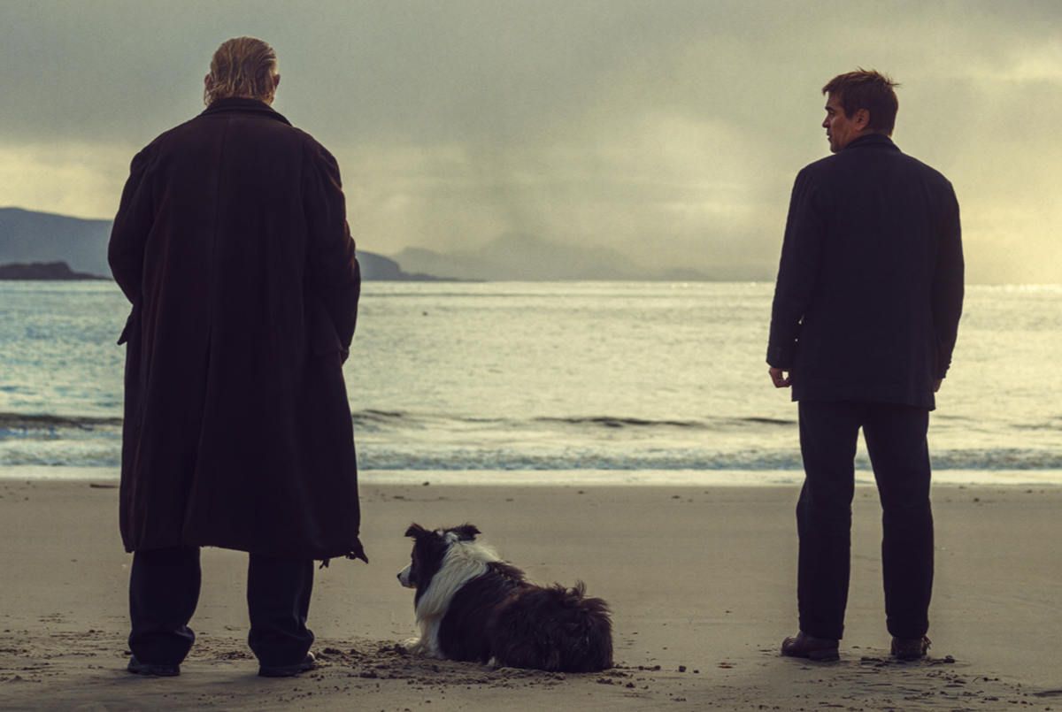 Brendan Gleeson, Colin Farrell and a very good border collie stand facing the sea in a still from THE BANSHEES OF INISHERIN.