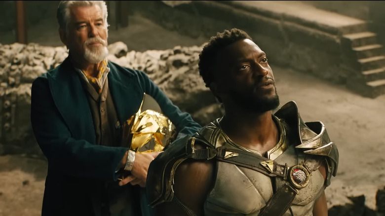 Surrounded by rubble, Doctor Fate (Pierce Brosnan) and Hawkman (Aldis Hodge) look skyward in a still from BLACK ADAM.
