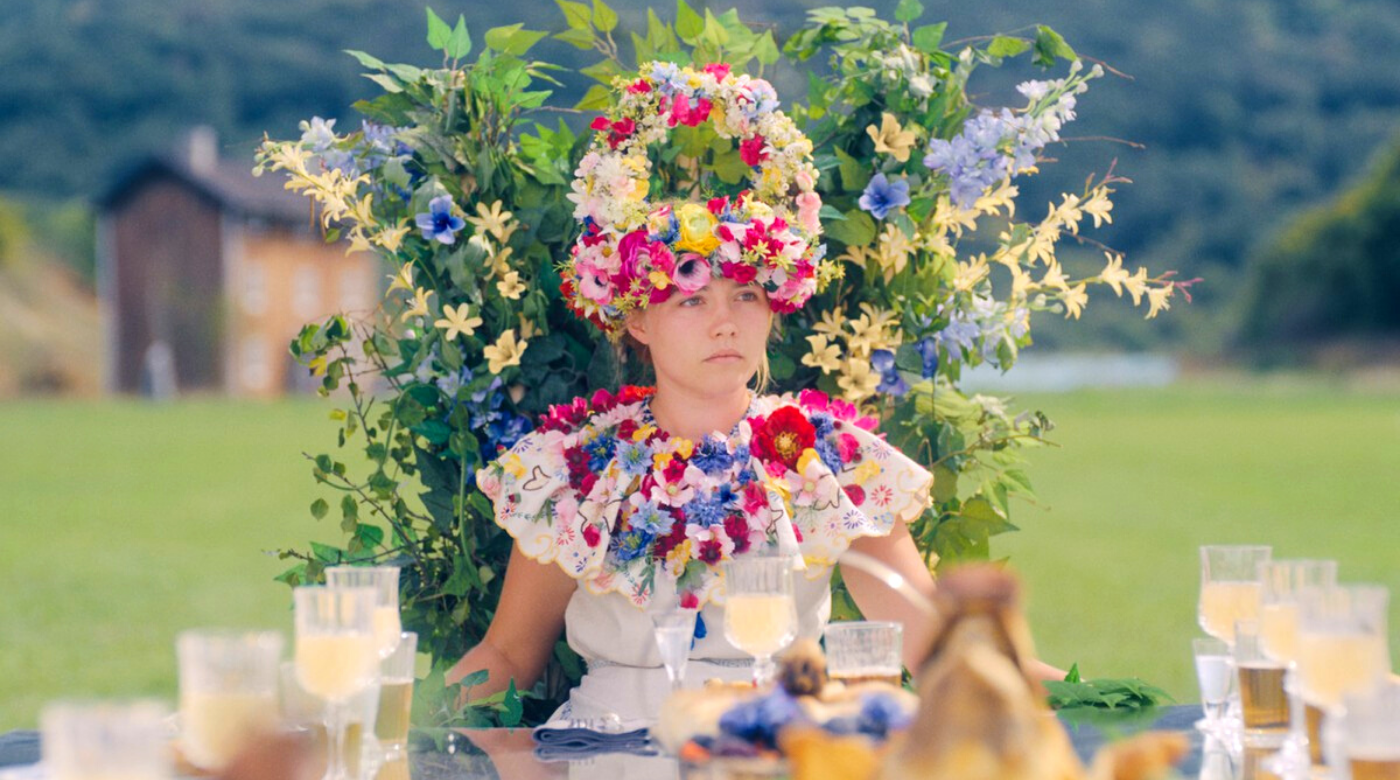 Florence Pugh, wearing a very silly floral crown, reacts to some bad news in Ari Aster's MIDSOMMAR. 