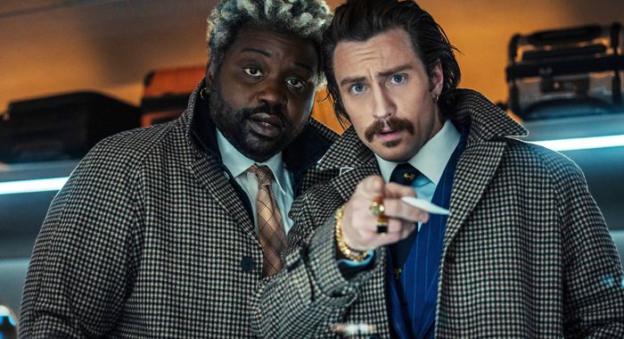 A still of BULLET TRAIN's Brian Tyree Henry and Aaron Taylor-Johnson, in matching overcoats.